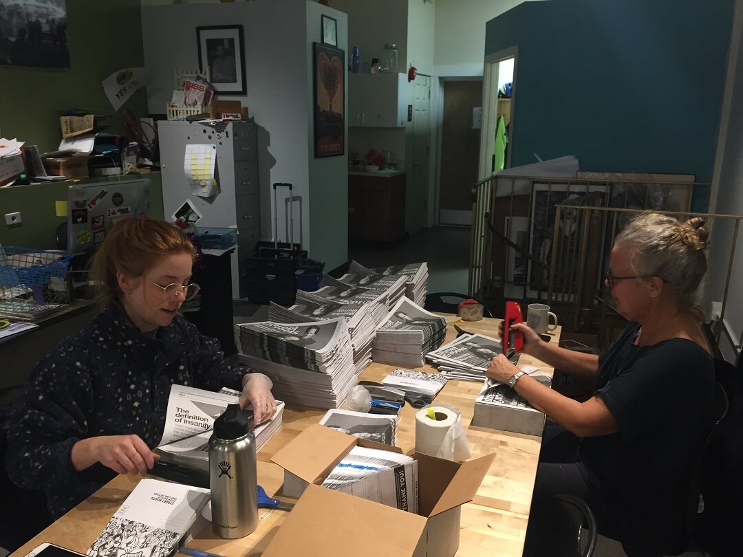 Street Roots volunteers work stuffing newspapers with donation envelopes 